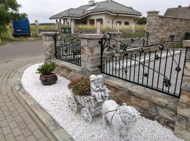 Ogród przed domem z kamieniem ozdobnym przy ogrodzeniu