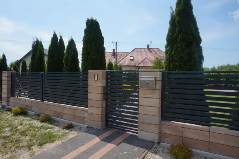 Ogrodzenie z dekoracyjnymi słupkami z bloczków i zielenią przy wejściu